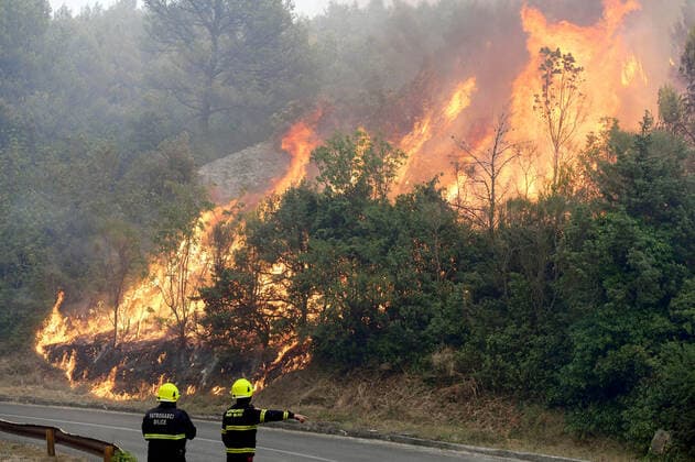 PXL_Zaton fire by the road Fire in an open area near the Zaton site in the Vodice hinterland, Croatia on July 13, 2022. About 30 firefighters with a dozen vehicles are on the ground, and two Canadairs joined the ground forces in extinguishing the fire. There are pine forests above, low vegetation, and endangered buildings. HrvojexJelavic PIXSELL