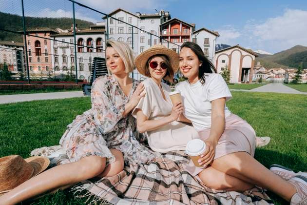 IMAGO Creative: Sommer, Sommertage im Stadtpark Smiling women with disposable coffee cups sitting on picnic blanket at park model released, Symbolfoto, OMIF00871