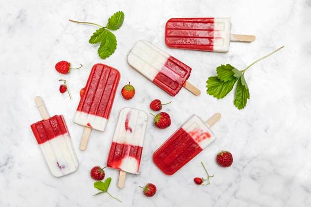 Homemade strawberry-yogurt popsicles flat laid against white marble, GWF07449