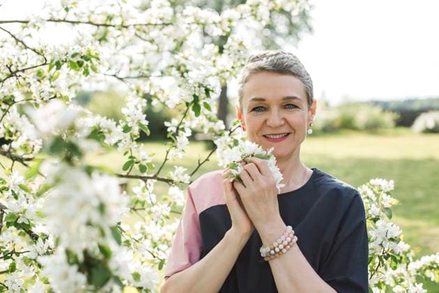 IMAGO Creative, Jahreszeit Frühling, Licht und Sonne Smiling woman holding white flower standing in garden model released, Symbolfoto, LLUF00686