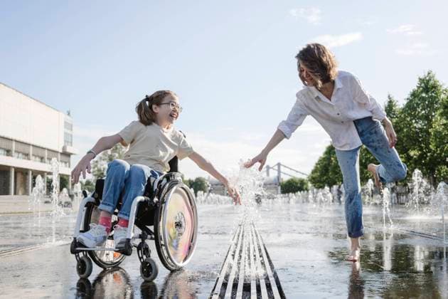 Woman and daughter with disability playing along fountain at park on sunny day model released, Symbolfoto, EYAF01970