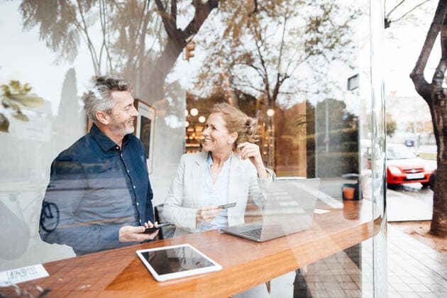 Smiling businesswoman holding credit card talking with man in cafe seen through window model released, Symbolfoto property released, JOSEF10817