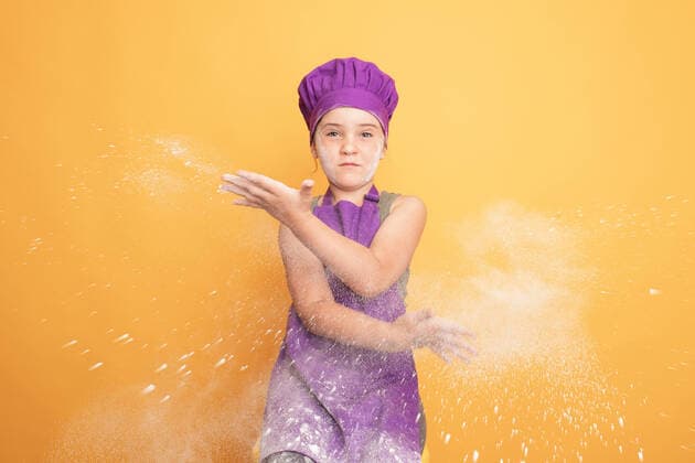 Creative Highlights Symbolbilder Optimistic girl in purple chef uniform clapping hands with white flour while sitting against yellow background in modern light studio looking at camera, Model released HodeiUnzueta_LittleChefs_00051.jpg Copyright: xHodeixUnzuetax MR