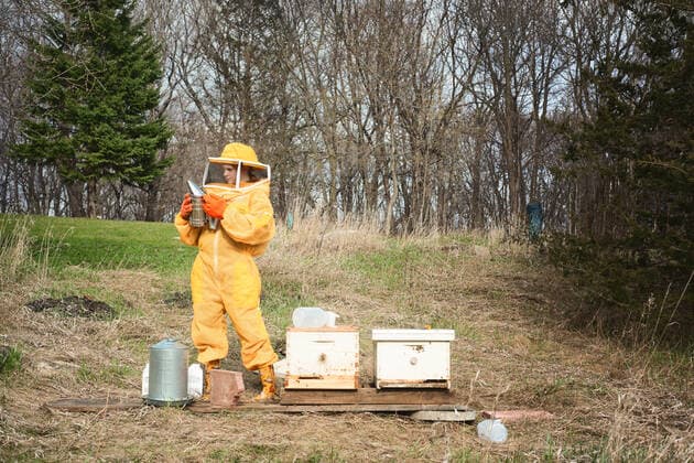 Creative Highlights Symbolbilder Girl in beekeeping suit standing by two hives with a smoker. Rockford, Minnesota, United States CR_RDOL220517-973618-01 EDITORIAL USE ONLY