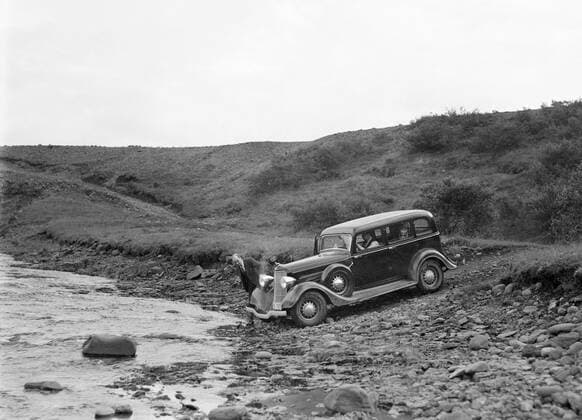 Poll photo collection. Iceland. Car at a stream to a narrow road in a rocky landscape. One of the passengers carefully takes a look at the front of the car. 1934. Iceland Copyright: xpiemagsx pienatarchpart630102021-18625 !ACHTUNG AUFNAHMEDATUM GESCHÄTZT!