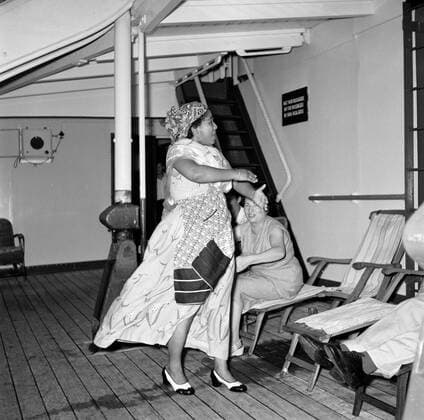 Poll photo collection. Netherlands Antilles and Suriname at the time of the royal visit of Queen Juliana and Prince Bernhard in 1955. Mrs. Snijders dressed as Surinamese dances on the MS. Nestor on the way to Suriname. In the background Mrs. Van de Poll. October 1, 1955 Copyright: xpiemagsx pienatarchpart630102021-23035 !ACHTUNG AUFNAHMEDATUM GESCHÄTZT!
