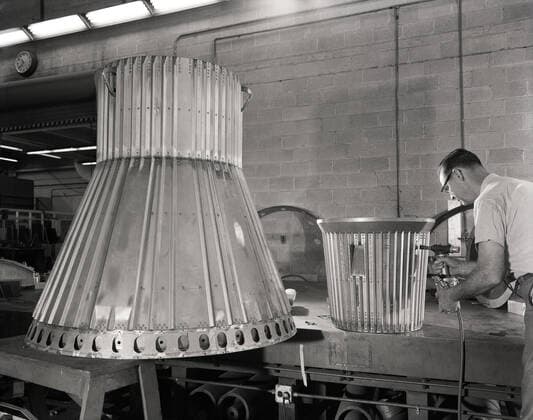 Assembling the Little Joe capsules. The capsules were manufactured in-house by Langley technicians. Three capsules are shown here in various stages of assembly. The escape tower and rocket motors shown on the completed capsule would be removed before shipping and finally assembly for launching at Wallops Island. Joseph Shortal wrote (vol. 3, p. 32): Design of the Little Joe capsules began at Langley before McDonnell started on the design of the Mercury capsule and was, therefore, a separate design. Although it was not designed to carry a man, it did have to carry a monkey. It had to meet the weight and center of gravity requirements of Mercury and withstand the same aerodynamic loads during the exit trajectory. Although in comparison Copyright: xpiemagsx piemagsspace-662 !ACHTUNG AUFNAHMEDATUM GESCHÄTZT!