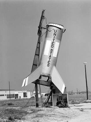 Testing of the Little Joe booster on its launcher. The launcher is positioned at its normal launch angle of 80 degrees. Joseph Shortal wrote (vol. 3, p. 33): The Little Joe booster was assembled at Wallops on its special launcher in a vertical attitude. It is shown in the on the left with the work platform in place. The launcher was located on a special concrete slab in Launching Area 1. The capsule was lowered onto the booster by crane.... After the assembly was completed, the scaffolding was disassembled and the launcher pitched over to its normal launch angle of 80 degrees.... Little Joe had a diameter of 80 inches and an overall length, including the capsule and escape tower of 48 feet. The total weight at launch was about 43,000 pou Copyright: xpiemagsx piemagsspace-670 !ACHTUNG AUFNAHMEDATUM GESCHÄTZT!