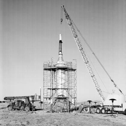 The Mercury capsule and escape tower are being lowered onto the Little Joe booster for launch on August 21, 1959. Joseph Shortal described this as follows (vol. 3, p. 33): The Little Joe booster was assembled at Wallops on its special launcher in a vertical attitude. It is shown in the on the left with the work platform in place. The launcher was located on a special concrete slab in Launching Area 1. The capsule was lowered onto the booster by crane.... After the assembly was completed, the scaffolding was disassembled and the launcher pitched over to its normal launch angle of 80 degrees.... Little Joe had a diameter of 80 inches and an overall length, including the capsule and escape tower of 48 feet. The total weight at launch was ab Copyright: xpiemagsx piemagsspace-709 !ACHTUNG AUFNAHMEDATUM GESCHÄTZT!