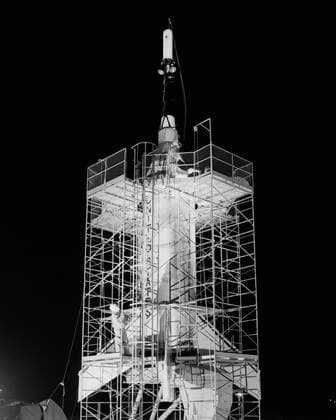 The Mercury capsule and escape tower are being lowered onto the Little Joe booster for launch on August 21, 1959. Joseph Shortal described this as follows (vol. 3, p. 33): The Little Joe booster was assembled at Wallops on its special launcher in a vertical attitude. It is shown in the on the left with the work platform in place. The launcher was located on a special concrete slab in Launching Area 1. The capsule was lowered onto the booster by crane.... After the assembly was completed, the scaffolding was disassembled and the launcher pitched over to its normal launch angle of 80 degrees.... Little Joe had a diameter of 80 inches and an overall length, including the capsule and escape tower of 48 feet. The total weight at launch was ab Copyright: xpiemagsx piemagsspace-710 !ACHTUNG AUFNAHMEDATUM GESCHÄTZT!