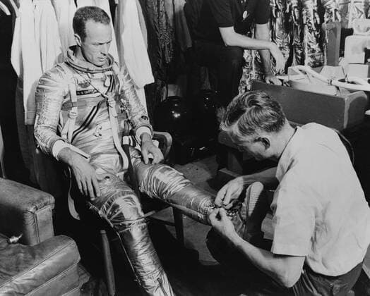 S61-03513 (1961) --- Mercury astronaut M. Scott Carpenter, prime pilot for the Mercury-Atlas 7 (MA-7) spaceflight, and Crew Equipment Specialist Joe Schmidt are pictured during a suiting exercise. Schmidt is seen lacing up Carpenter s boots. Copyright: xpiemagsx piemagsspace-894 !ACHTUNG AUFNAHMEDATUM GESCHÄTZT!