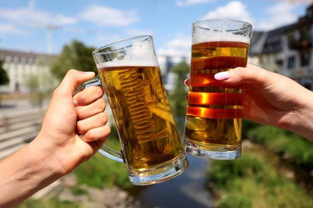 Zwei Bierglaeser mit Haenden stossen vor blauem Himmel in der Siegener Innenstadt an. Siegufer im Hintergrund.. Sommer im Siegerland am 04.08.2022 in Siegen Deutschland. *** Two beer glasses with hands bumping against blue sky in Siegen city center Siegufer in background summer in Siegerland on 04 08 2022 in Siegen Germany