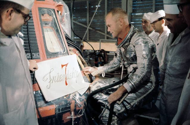 S64-14854 (20 Feb. 1962) --- Astronaut John H. Glenn Jr. and technicians inspect a decal ready for application to the side of his Mercury spacecraft prior to launch on Feb. 20, 1962. The decal reads Friendship 7 . Copyright: xpiemagsx piemagsspace-115587 !ACHTUNG AUFNAHMEDATUM GESCHÄTZT!