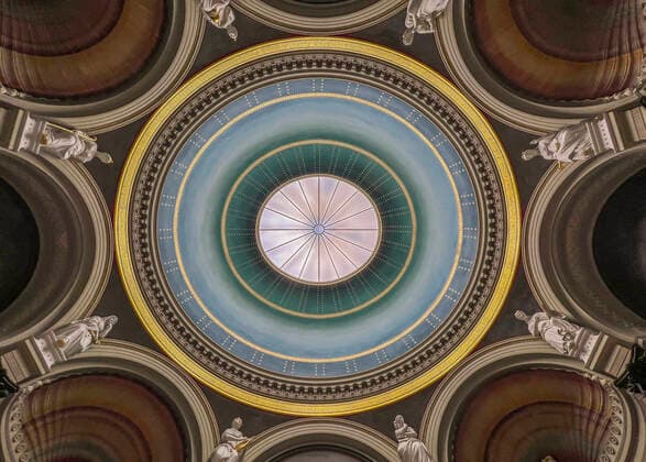 Der Kuppelsaal in der Alten Nationalgalerie auf der Museumsinsel in Berlin-Mitte. Aus der Öffnung in der Mitte der Kuppel fällt das Licht auf weiße Figuren zwischen den Bögen. Im Zweiten Weltkrieg wurde der Saal durch einen Bombentreffer stark beschädigt. Bei der Sanierung der Nationalgalerie in den Jahren 1999 bis 2001 wurden die ursprünglichen Wandfarben rekonstruiert. Foto: Volker Hohlfeld Kuppelhalle Alte Nationalgalerie