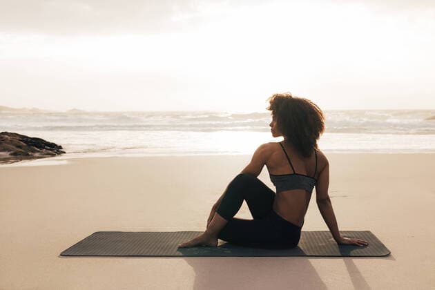 Creative Highlights Symbolbilder Side view of woman sitting on mat. Female meditating on seashore at sunset. Copyright: xArtemxVarnitsinxArtemxVarnitsinx