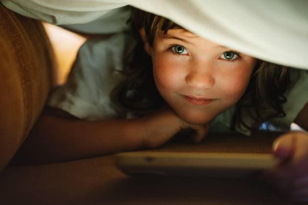 IMAGO Creative, Weihnachten, Tradition: Weihnachtsfilme sehen Creative Highlights Symbolbilder Girl under a blanket using a mobile phone at home looking at camera, Model released HodeiUnzueta_KidsHome_00095.jpg Copyright: xHodeixUnzuetax MR