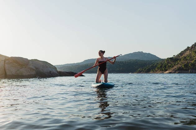 IMAGO Creative: 2022 Sport Favoriten IMAGO Creative: Ende des Sommers Full body of active female in swimwear floating on paddleboard in rippling lake against rock and shore with forest on summer day, Model released MiguelPalomo_WomanWithPaddleSurfInLake_11.jpg Copyright: xMiguelxPalomox MR