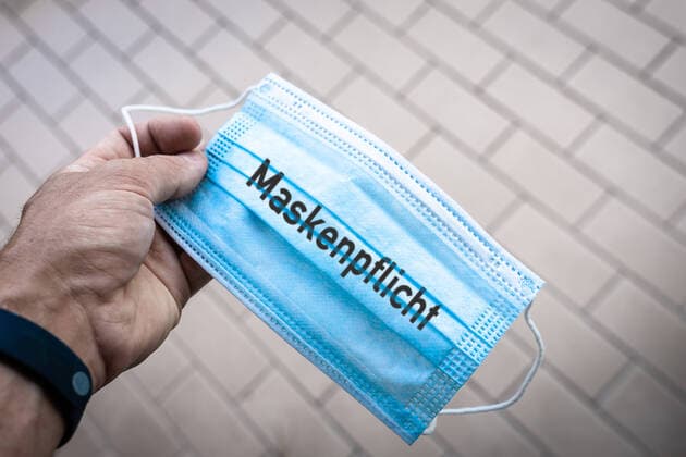 Eine Hand hält eine Covid 19 Coronavirus Schutzmaske mit Aufschrift: Maskenpflicht. Maske und Maskenpflicht Symbolbild FOTOMONTAGE