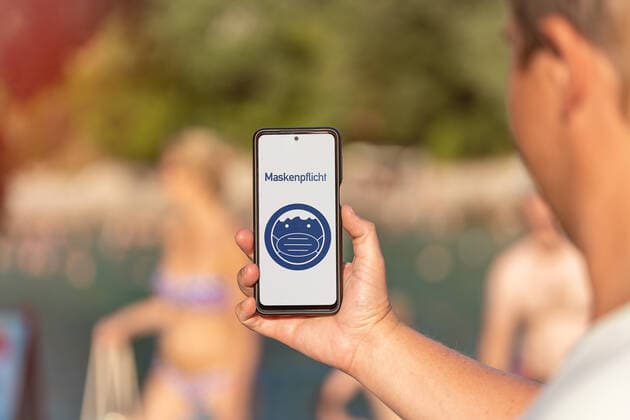 Mann hält Smartphone in der Hand mit dem Hinweis Maskenpflicht auf dem Bildschirm. Pflicht zum Tragen einer Maske, Schutzmaske FOTOMONTAGE