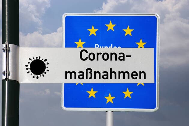 Symbolbild Coronamaßnahmen: Straßenschild mit der Aufschrift Coronamaßnahmen vor einem deutschen Grenzschild