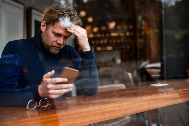 Worried businessman using smart phone in cafe seen through glass window model released, Symbolfoto property released, JOSEF11052