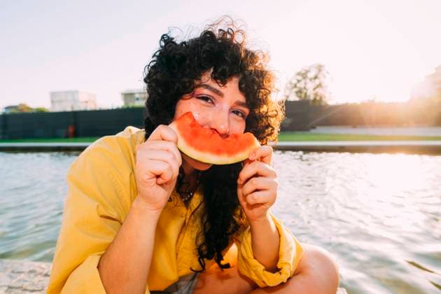 Young woman eating watermelon by pond at sunset model released, Symbolfoto, MEUF07542