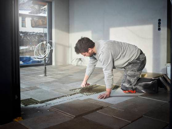 Young tiler applying adhesive on floor at construction site model released, Symbolfoto property released, CVF02115