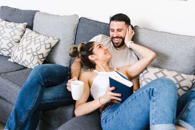 Content ethnic couple sitting on sofa together while looking at each other and relaxing at weekend at home, Model released, Property released MarcosCastillo_LatinYoungCouple_4 Copyright: xMarcosxCastillox MR