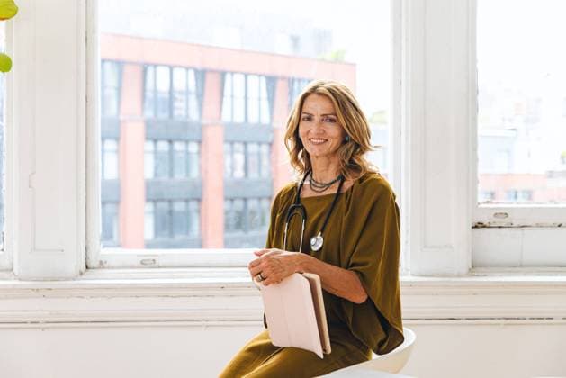 IMAGO Creative: Lokalhelden - Gesundheits- und Rettungskräfte Portrait of smiling mature female doctor sitting in front of window New York, New York, United States CR_LIWEEE220831-1036973-01 ,model released, Symbolfoto ,property released
