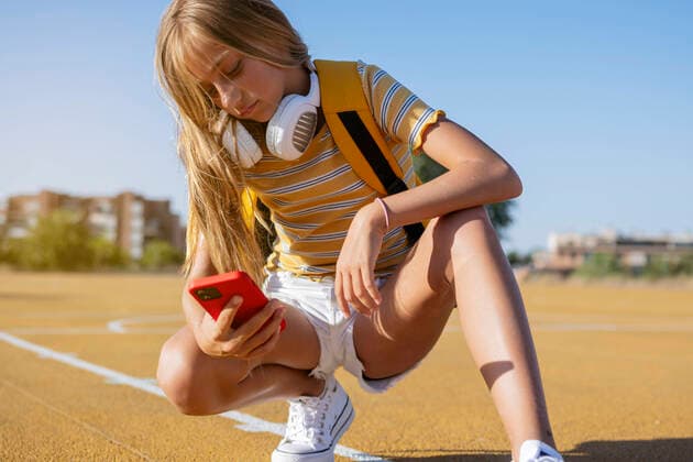 IMAGO Creative: 2022 Sport Favoriten IMAGO Creative: Lokalhelden - Jugendsportbildung Full body of focused teenage girl with headphones texting message on cellphone while standing on playground with basketball hoop on summer day, Model released JoseLuisCarrascosa_ID441_16829_014 Copyright: xJosexLuisxCarrascosax MR
