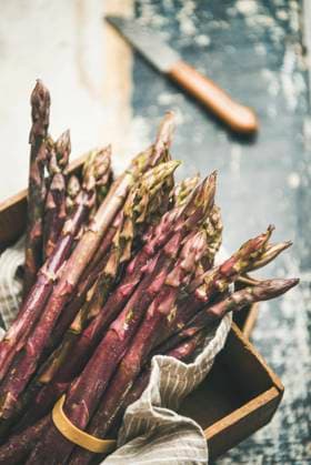 Fresh raw uncooked purple asparagus, selective focus Seasonal harvest produce. Fresh raw uncooked purple asparagus over wooden tray background, selective focus, vertical composition. Local market food concept Copyright: xAnnaxIvanovax AI290618-6