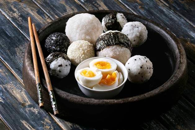 Rice balls and eggs Stone tray with different size rice balls with black sesame and seaweed nori, served with soft boiled eggs and chopsticks over wooden plank background. Asian style dinner. Copyright: xNatashaxBreenx NB161017-69