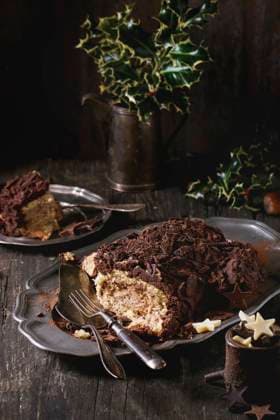 Sliced christmas chocolate yule log Sliced homemade Christmas chocolate yule log with chestnuts cream on vintage plate with forks, chocolate stars and holly branch over old wooden table. Dark rustic style. Copyright: xNatashaxBreenx NB271016-6