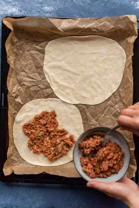 Woman making lahmacun from scratch with homemade dough and ground beef filling on a parchment paper lined baking sheet. Copyright: xYusufxRizaxGunaydinx YG100720-7