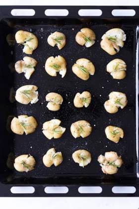 Smashed potatoes with black pepper and rosemary in a baking sheet. Copyright: xYusufxRizaxGunaydinx YG230520-16