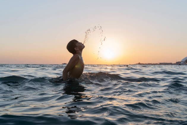 Creative Highlights Symbolbilder A boy jumps into the sea at sunset splashing water from his mouth. Sochi, Krasnodar Krai, Russia CR_OWQV220908-1039880-01 ,model released, Symbolfoto