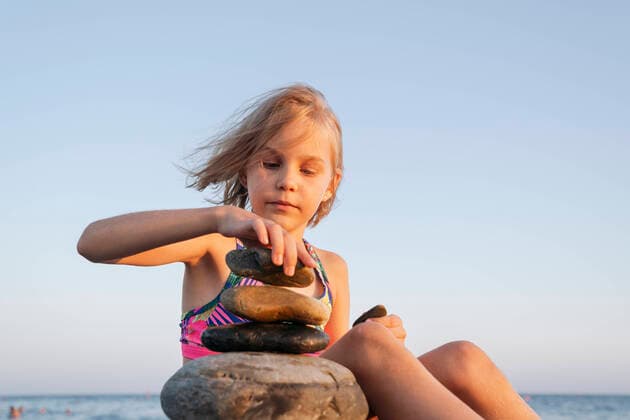 Creative Highlights Symbolbilder A girl sits on the seashore at sunset and plays with stones. Sochi, Krasnodar Krai, Russia CR_OWQV220908-1039881-01 ,model released, Symbolfoto