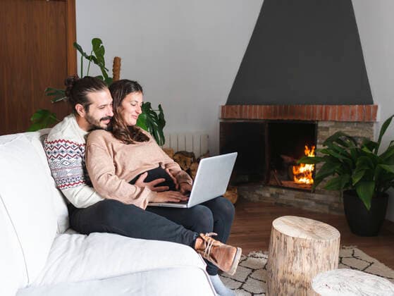 IMAGO Creative: Herbst, Gemütliches Zuhause Side view full body of loving couple using laptop while sitting together on sofa placed near fireplace in modern apartment, Model released AlbertMorcillo_PlantDecorationFamily_41 Copyright: xAlbertxMorcillox MR