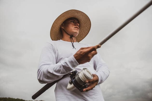 Creative Highlights Symbolbilder From below male in hat with fishing rod catching fish on sandy shore, Model released CristianRojas_ShoreFishing_53 Copyright: xCristianxRojasx MR