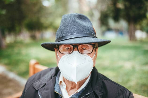 Creative Highlights Symbolbilder Aged man wearing protective mask with hat looking at camera while sitting on wooden bench in park on blurred background, Model released DaniNavarro_97YearsOld_16 Copyright: xDanixNavarrox MR
