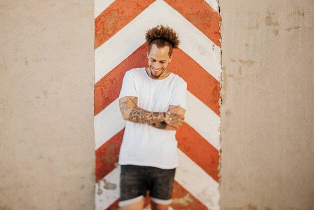 Creative Highlights Symbolbilder Positive young ethnic man in casual clothes smiling with closed eyes while leaning on weathered wall on city street, Model released GustavoPozo_EddieAndMarta_39 Copyright: xGustavoxPozox MR