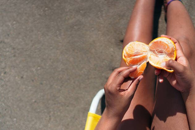 Creative Highlights Symbolbilder Anonymous hispanic female peeling fresh orange while relaxing on deckchair at seaside and enjoying summer vacation, Model released HectorPertuz_WomanOnBeach_22 Copyright: xHectorxPertuzx MR