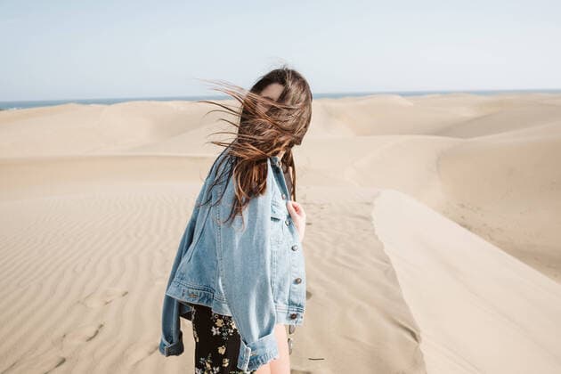 Creative Highlights Symbolbilder Side view of anonymous young woman with hair covered by wind standing on sand dune between desert and blue heaven in evening in Canary Islands, Spain, Model released JakeJakab_CanaryTravels_34 Copyright: xJakexJakabx MR