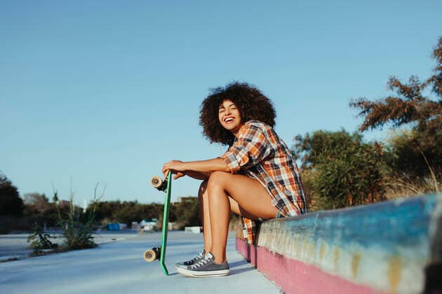 Creative Highlights Symbolbilder Side view of calm black female with in trendy summer outfit and with afro hairstyle sitting on stone border with green penny board and looking at camera, Model released Lightsy_SkaterGirl_23 Copyright: xLightsyx MR