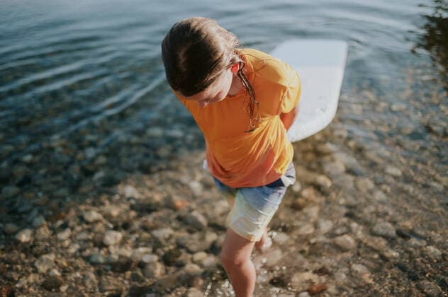 Creative Highlights Symbolbilder Boy carries white paddle board on to shore of rocky lake Traverse City, Michigan, United States CR_LICE220912-1041173-01 ,model released, Symbolfoto