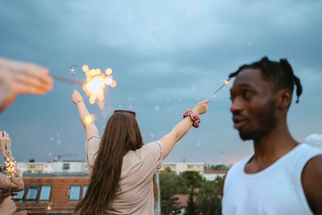 IMAGO Creative: Guten Rutsch Creative Highlights Symbolbilder Rear view of woman with arms raised holding lit sparklers against sky Germany, Berlin, model released Copyright: xMaskot,xMaskotxBildbyraxABx , MA95152 MA95152