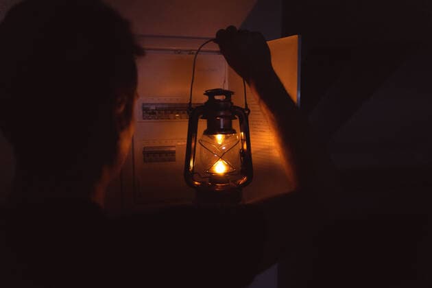 Bavaria, Germany - 25 September 2022: Power failure in the apartment, man lights with lantern and candlelight and checks the fuse box. electricity, power outage, blackout concept *** Stromausfall in der Wohnung, Mann leuchtet mit Laterne und Kerzenlicht und überprüft den Sicherungskasten. Elektrizität, Strom Ausfall, Blackout Konzept