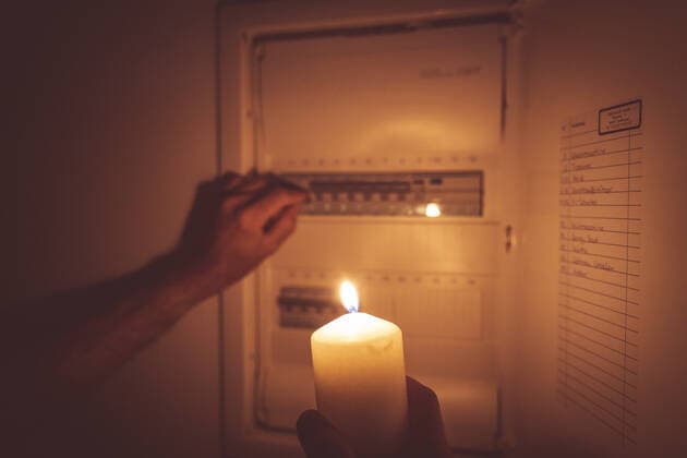 Bavaria, Germany - 25 September 2022: Power failure in the apartment, man lights with candle and candlelight and checks the fuse box. electricity, power outage, blackout concept *** Stromausfall in der Wohnung, Mann leuchtet mit Kerze und Kerzenlicht und überprüft den Sicherungskasten. Elektrizität, Strom Ausfall, Blackout Konzept