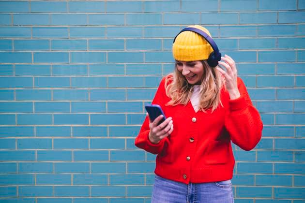 Happy young woman in wireless headphones using smart phone in front of wall model released, Symbolfoto, AMWF00313