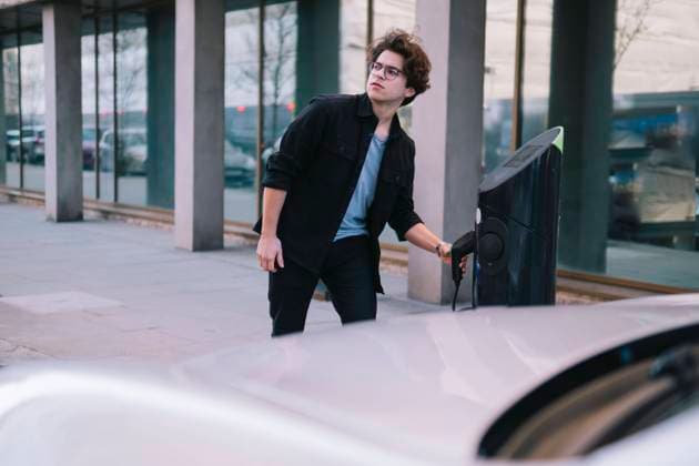 Young man pulling out electric plug at charging station model released, Symbolfoto, AMWF00366